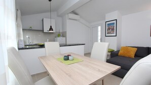 Een moderne keuken met witte kasten, een eettafel met stoelen en een grijze bank met een geel kussen.