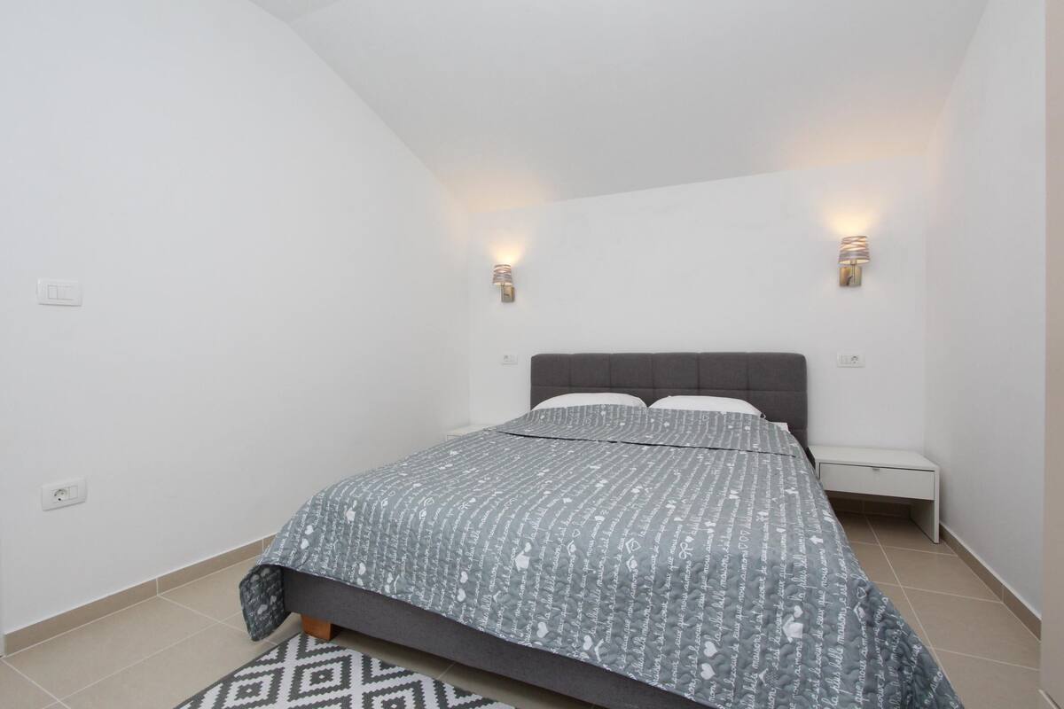 A bedroom with a bed, two bedside tables, and wall-mounted lights.