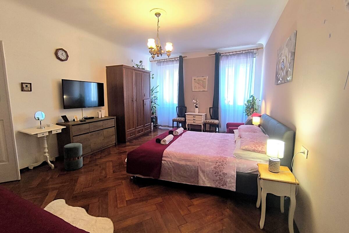 Een slaapkamer met een bed, nachtkastjes, een televisie, een kledingkast, een bureau en een stoel.