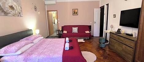 Una camera da letto con un letto, un divano rosso, una TV e un comò in legno.