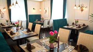 En restaurant med turkise polstrede bænke, pænt dækkede borde med vinglas og hængende lamper.