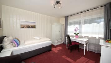 A bedroom with a bed, a desk, a chair, a wardrobe, and a window with curtains.