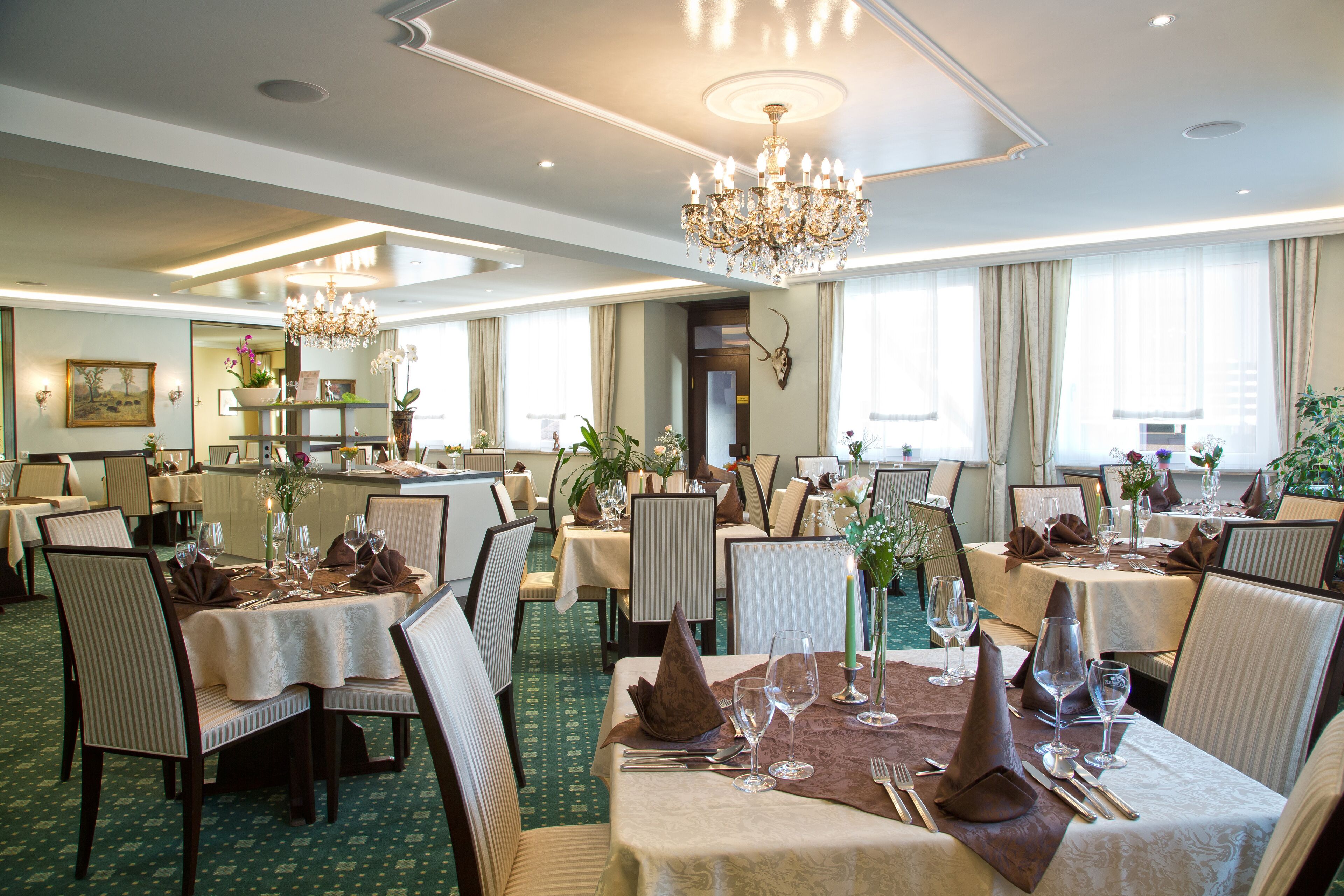 Un comedor de hotel con varias mesas dispuestas para comer, candelabros y un suelo cubierto de moqueta verde.