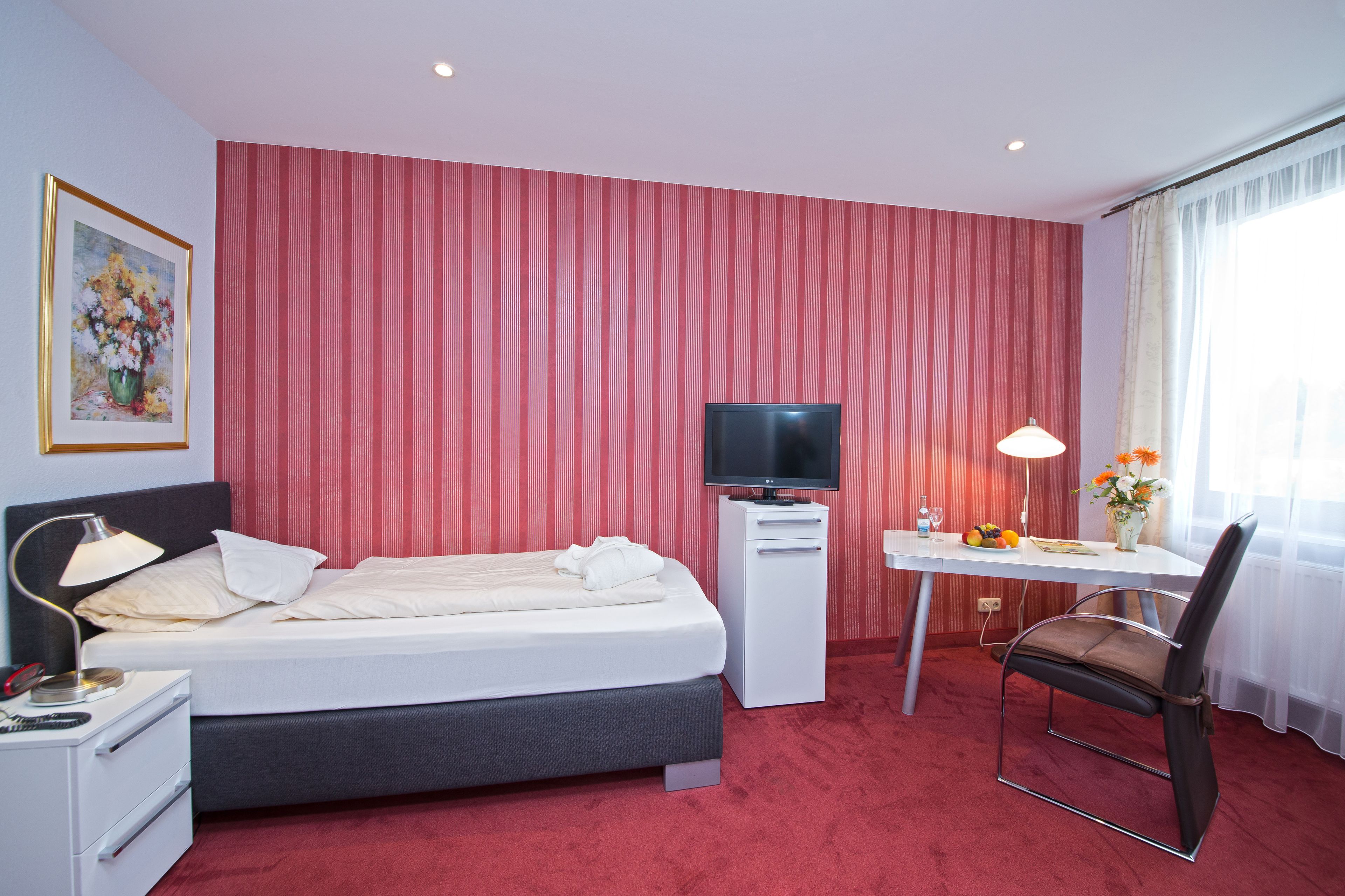 Ein Hotelzimmer mit Bett, Schreibtisch, Stuhl, Fernseher, Lampe und einem Gemälde an der Wand.