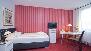 Ein Hotelzimmer mit Bett, Schreibtisch, Stuhl, Fernseher, Lampe und einem Gemälde an der Wand.
