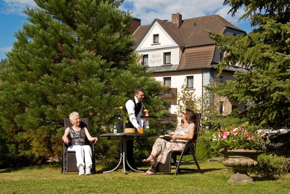 Un jardín con mesa y sillas, una persona de pie y un edificio al fondo.