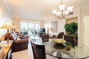 A modern living room with a glass coffee table, leather sofa, and a dining area with chairs.