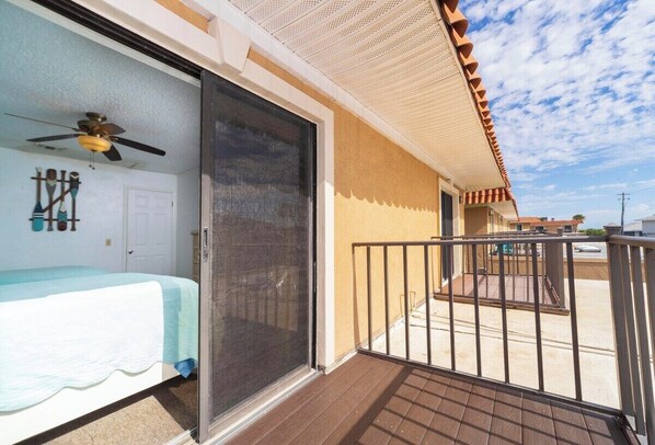Une chambre avec un lit, un ventilateur de plafond, une porte-fenêtre coulissante et un balcon doté d’une balustrade.