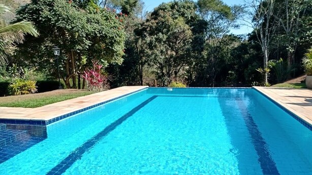 A rectangular swimming pool with clear blue water, surrounded by a tiled deck and lush greenery. - Amazing house in the mountains in a gated community, lots of privacy - Paty do Alferes (Paty do Alferes)