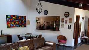 A living room with a brown leather sofa, a colorful abstract painting, a kitchen area, and a dining table with chairs. - Amazing house in the mountains in a gated community, lots of privacy - Paty do Alferes (Paty do Alferes)