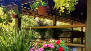 A covered outdoor area with hanging planters and a large potted plant with pink flowers. - Amazing house in the mountains in a gated community, lots of privacy - Paty do Alferes (Paty do Alferes)