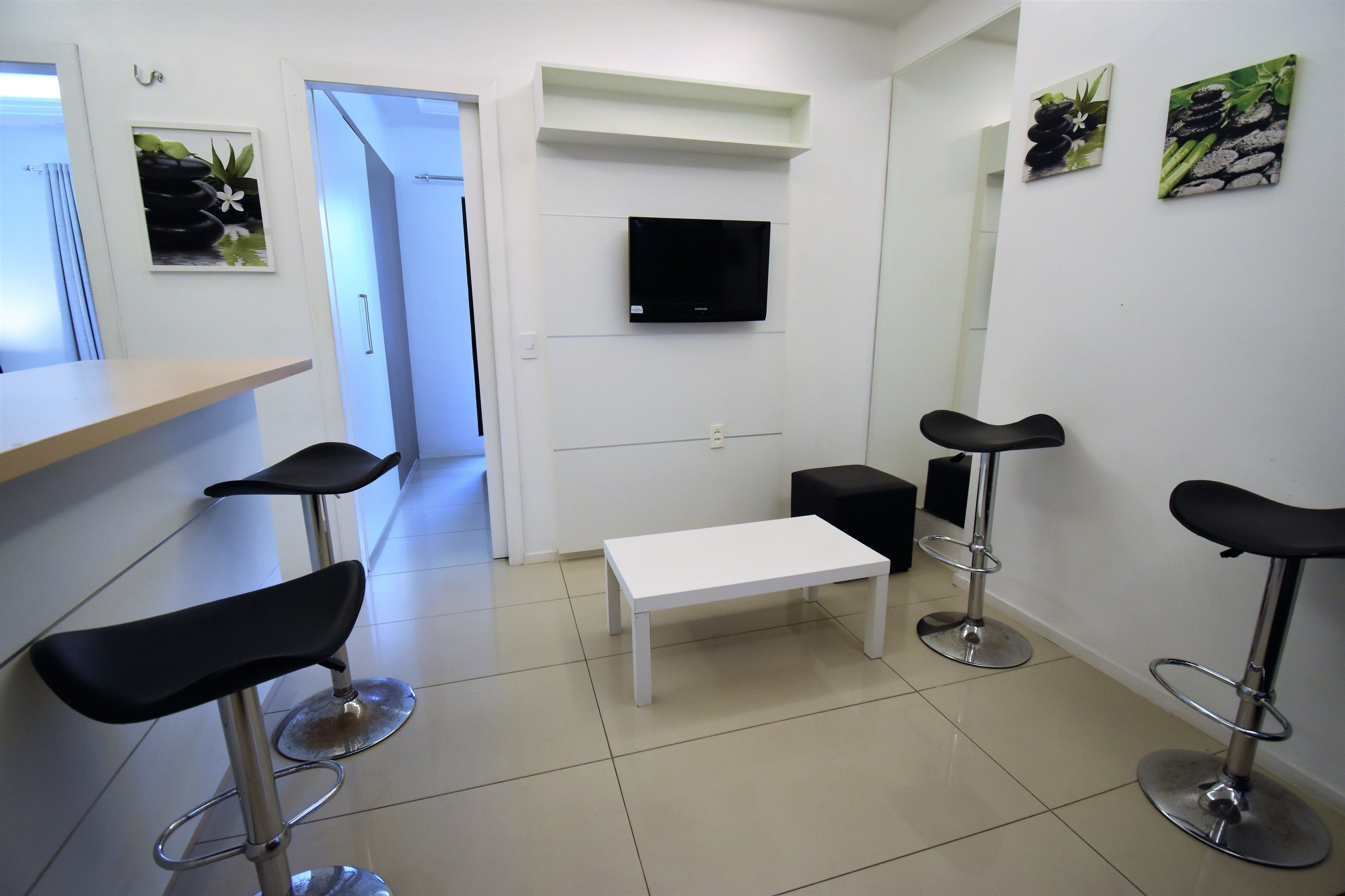 A modern bar area with a white bench, black bar stools, and a flat-screen TV mounted on the wall.