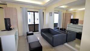 A modern living room with a sofa, a TV, and a glass coffee table. There is a large mirror on the wall and a sliding door leading to a balcony. - SEAFLATS Villa Costeira (Fortaleza)