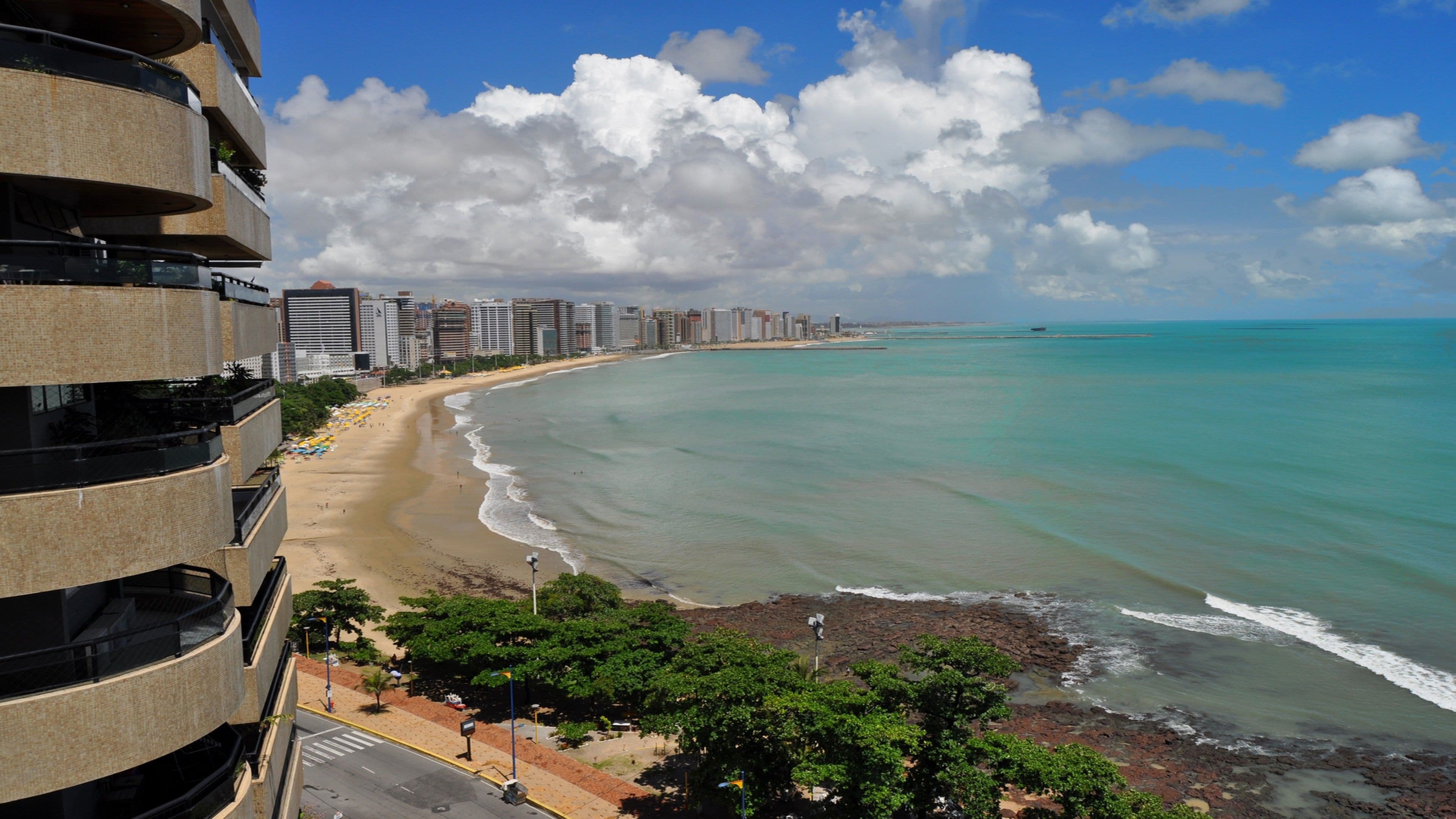 A beach with a view of a cityscape, including high-rise buildings and a clear sky.