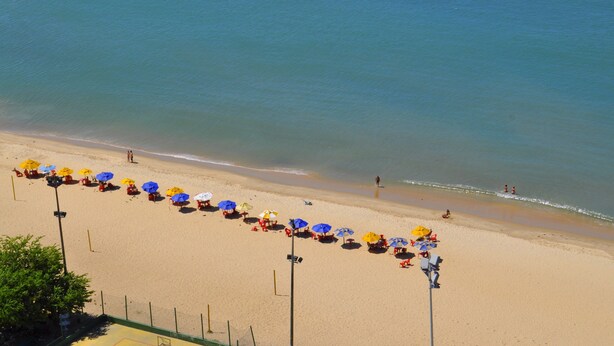 A beach with rows of umbrellas and beach chairs, a sandy shore, and a calm sea. - SEAFLATS Villa Costeira (Fortaleza)