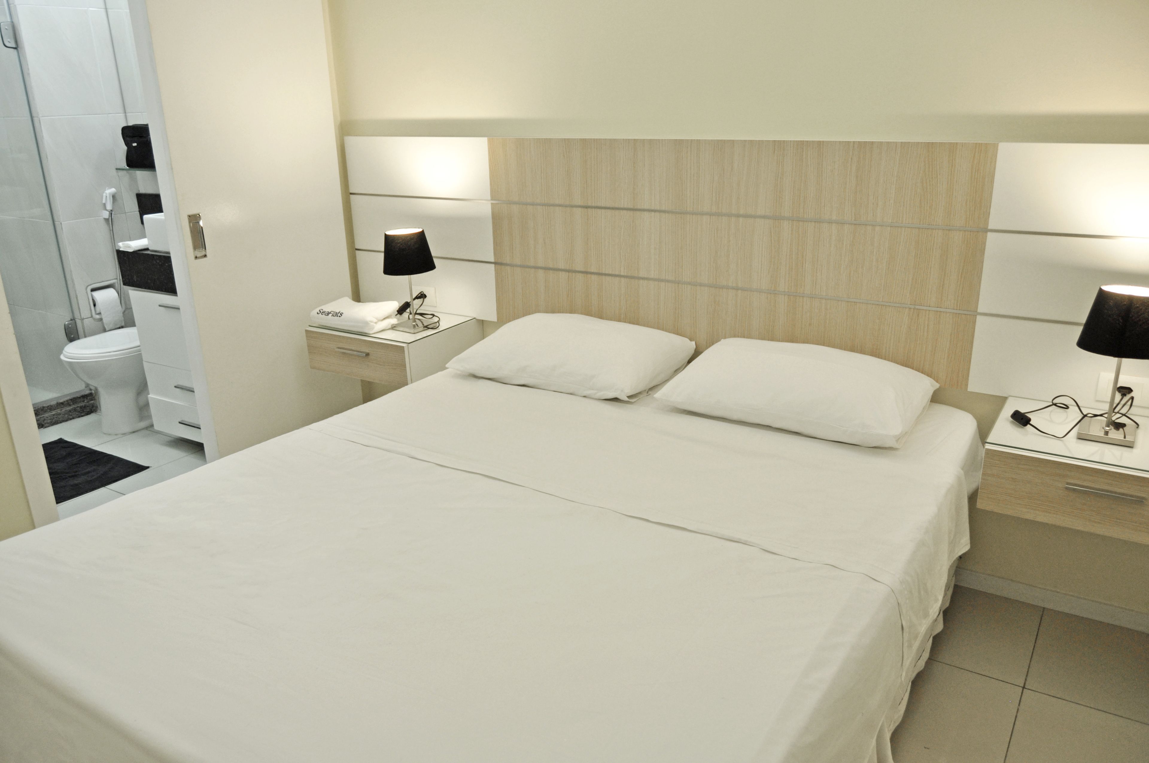 A hotel room with a large bed, two bedside tables with lamps, a small bedside table with a phone, and a bathroom visible through an open door.