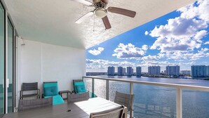 A balcony with a table and chairs, a ceiling fan, and a view of a city skyline across a body of water.