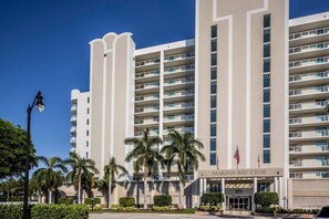 Een meerlaags hotel met een modern ontwerp, met balkons op elke verdieping en een opvallende entree met de naam 'Marina Bay Club'.