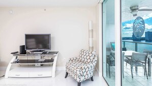 A modern living room with a flat-screen TV, a patterned armchair, and a glass table with chairs.
