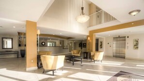 A spacious lobby with a high ceiling, a reception desk, seating area, and a staircase.
