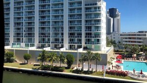 A multi-story hotel with balconies, a swimming pool, and palm trees.
