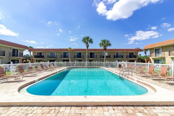A swimming pool with lounge chairs and a white fence, surrounded by buildings with red roofs and windows. - Panoramic Ocean Views at Ponce Landing 2 (St. Augustine)