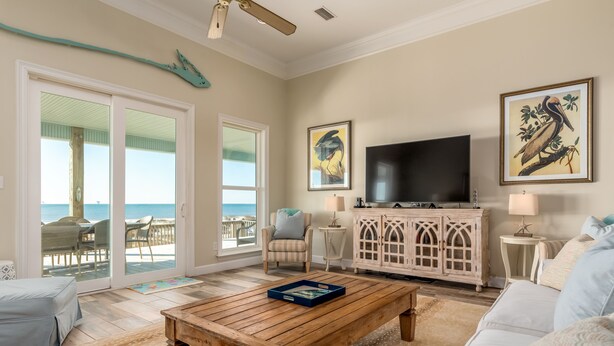 Un saló amb una taula baixa de fusta, un sofà blanc, una televisió i una vista a l'oceà a través de grans portes corredisses.