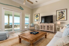 A living room with a wooden coffee table, a white sofa, a TV, and a view of the ocean through large sliding doors.