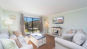 Een woonkamer met een bank, een salontafel, een televisie en een balkon met gordijnen.