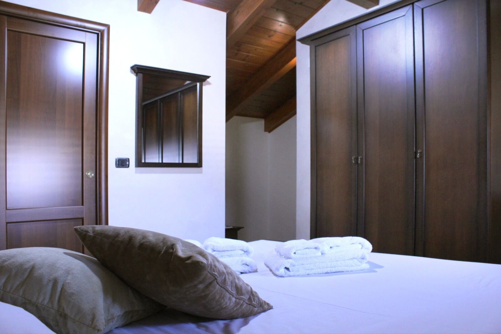 A bedroom with a bed, pillows, a mirror, and a wardrobe.
