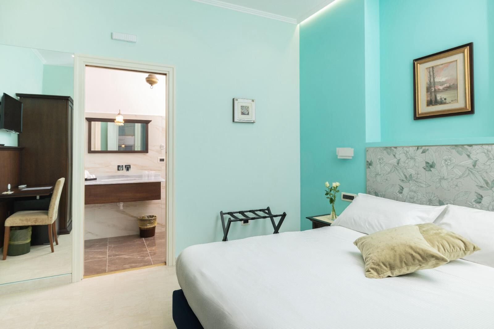 A bedroom with a bed, a desk, and a bathroom visible through an open door.