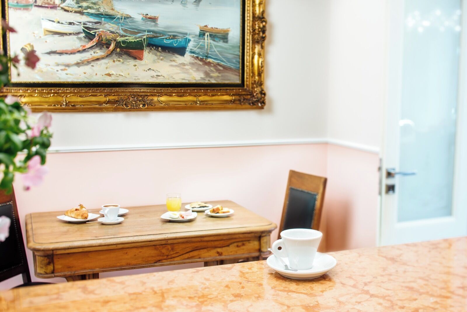Comedor con mesa de madera preparada para el desayuno, un cuadro en la pared y una puerta al fondo.