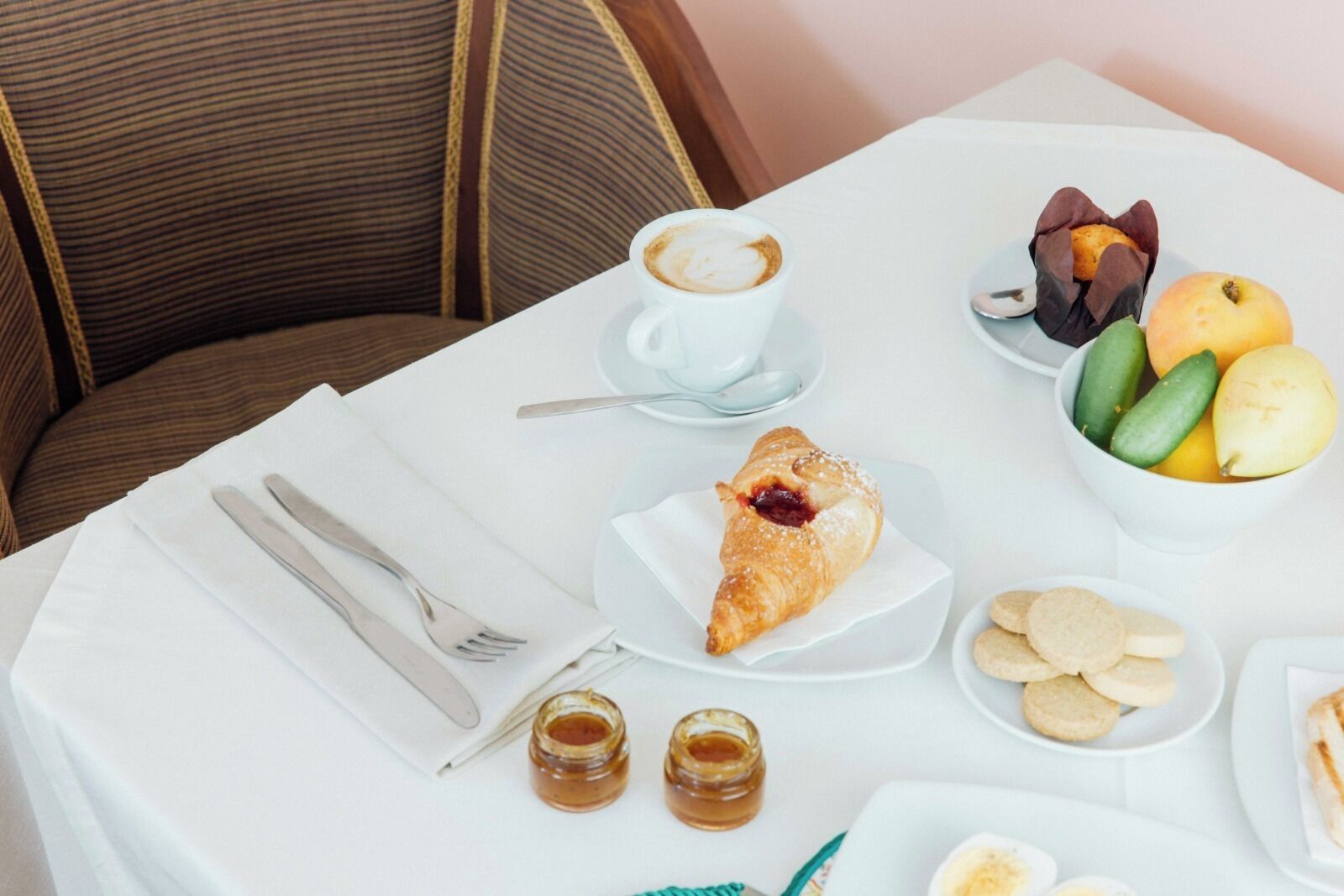 Colazione con croissant, caffè, frutta e biscotti su un tavolo bianco.