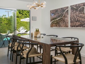 Un espace repas moderne avec une table en verre, des chaises foncées et une vue sur la verdure environnante.