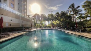 A swimming pool with clear water, surrounded by palm trees and a building with balconies. - Le Golden Bay 902 STR-00876 (Sunny Isles Beach)