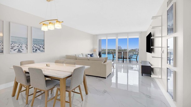 A modern living room with a dining area, large windows, and a view of the sea. - Le Golden Bay 902 STR-00876 (Sunny Isles Beach)