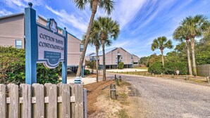 A gated entrance to Cotton Royal Condominiums with a clear sky and palm trees. - Orange Beach Resort Condo w/ Pool - Walk to Beach! (Orange Beach)