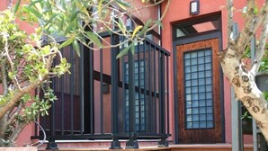 Una escalera de madera que conduce a una puerta con diseño de cuadrícula, rodeada de plantas en macetas y un muro rojo.