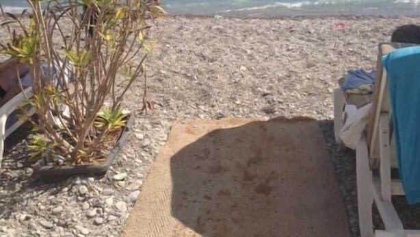 Una playa con un sendero de piedras que lleva a un área de descanso con sombrillas.