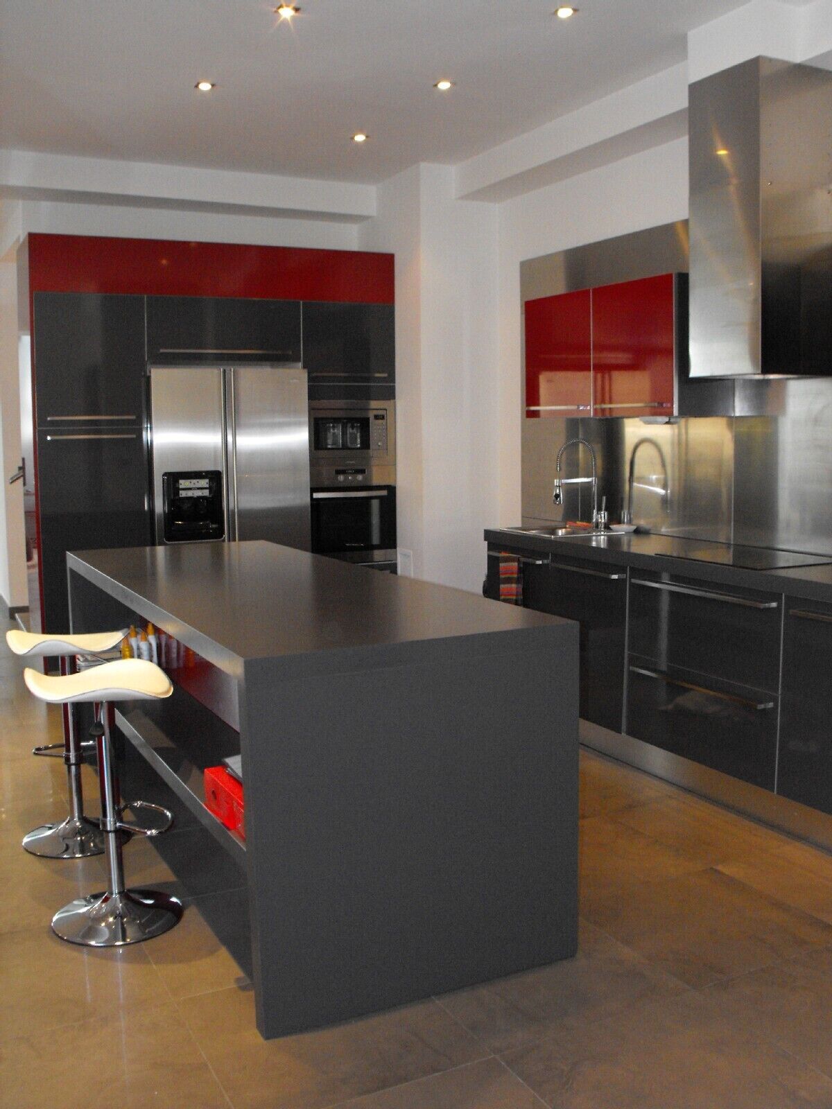 Une cuisine moderne dotée d’un îlot central, d’appareils électroménagers en acier inoxydable et de touches de couleur rouge.