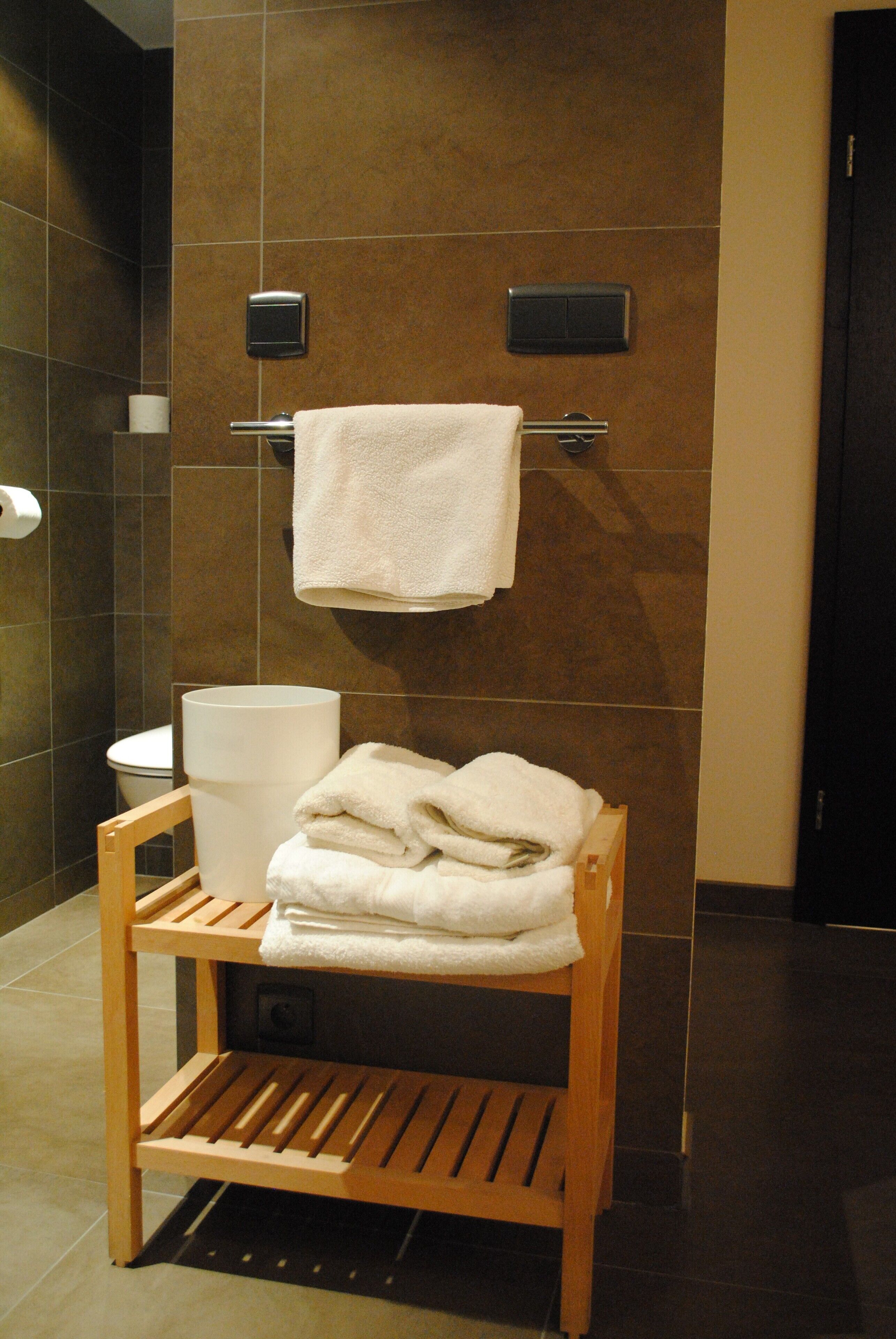A bathroom with a wooden bench, a stack of white towels, and two towel dispensers mounted on the wall.