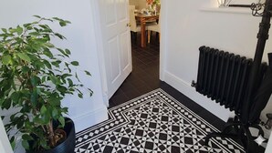 Un pasillo con suelo a cuadros blanco y negro, una planta en maceta, un radiador y una escalera que conduce a un comedor.
