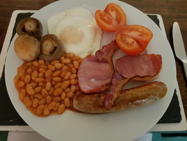 A plate of breakfast food including eggs, bacon, sausages, beans, mushrooms, and tomatoes. - Wisteria Haze (Bedford)