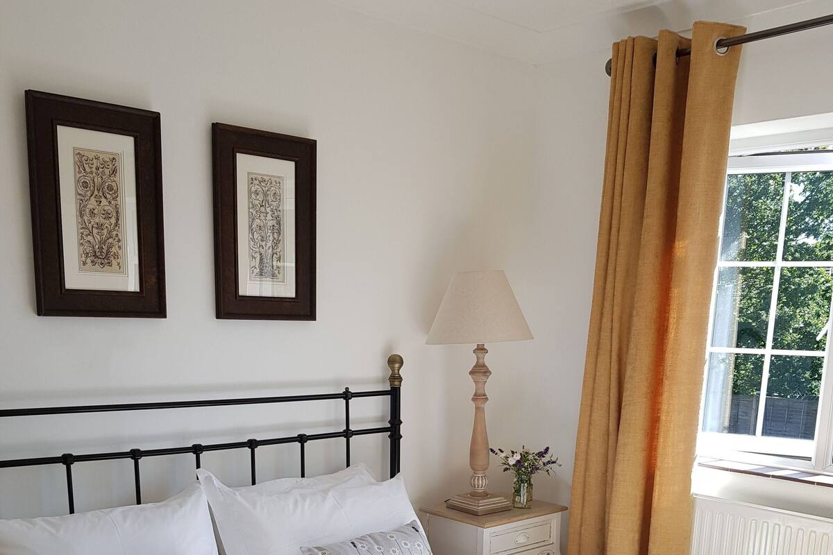 A neatly made bed with a floral quilt, a bedside table with a lamp, and two framed pictures on the wall.