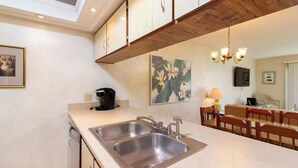 Une cuisine moderne dotée de deux éviers en acier inoxydable, de meubles en bois, d’une machine à café et d’un coin repas avec des chaises et une table en bois.