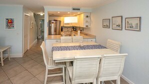 Comedor con mesa y sillas, cocina al fondo y un pasillo que lleva a otra habitación.