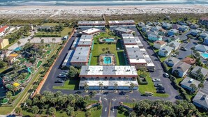 Vista aérea de un hotel costero con varias construcciones, una piscina central y una playa al fondo.