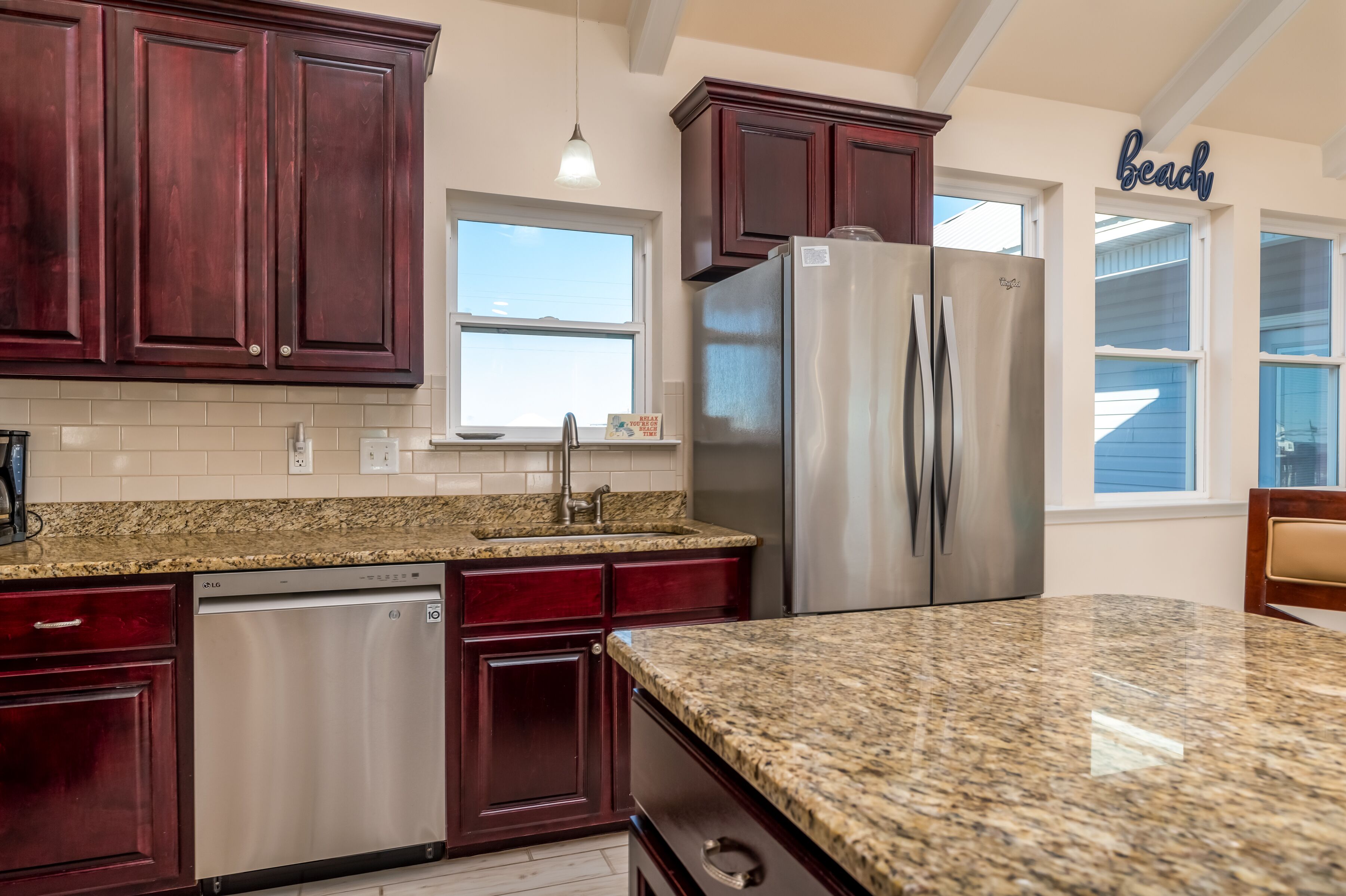 A kitchen with dark wood cabinets, a stainless steel refrigerator, granite countertops, and a window with a view.