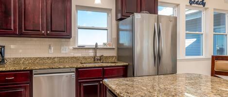 A kitchen with dark wood cabinets, a stainless steel refrigerator, granite countertops, and a window with a view.