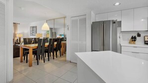 Una cocina moderna con armarios blancos, un refrigerador de acero inoxidable y un comedor con mesa y sillas de madera.